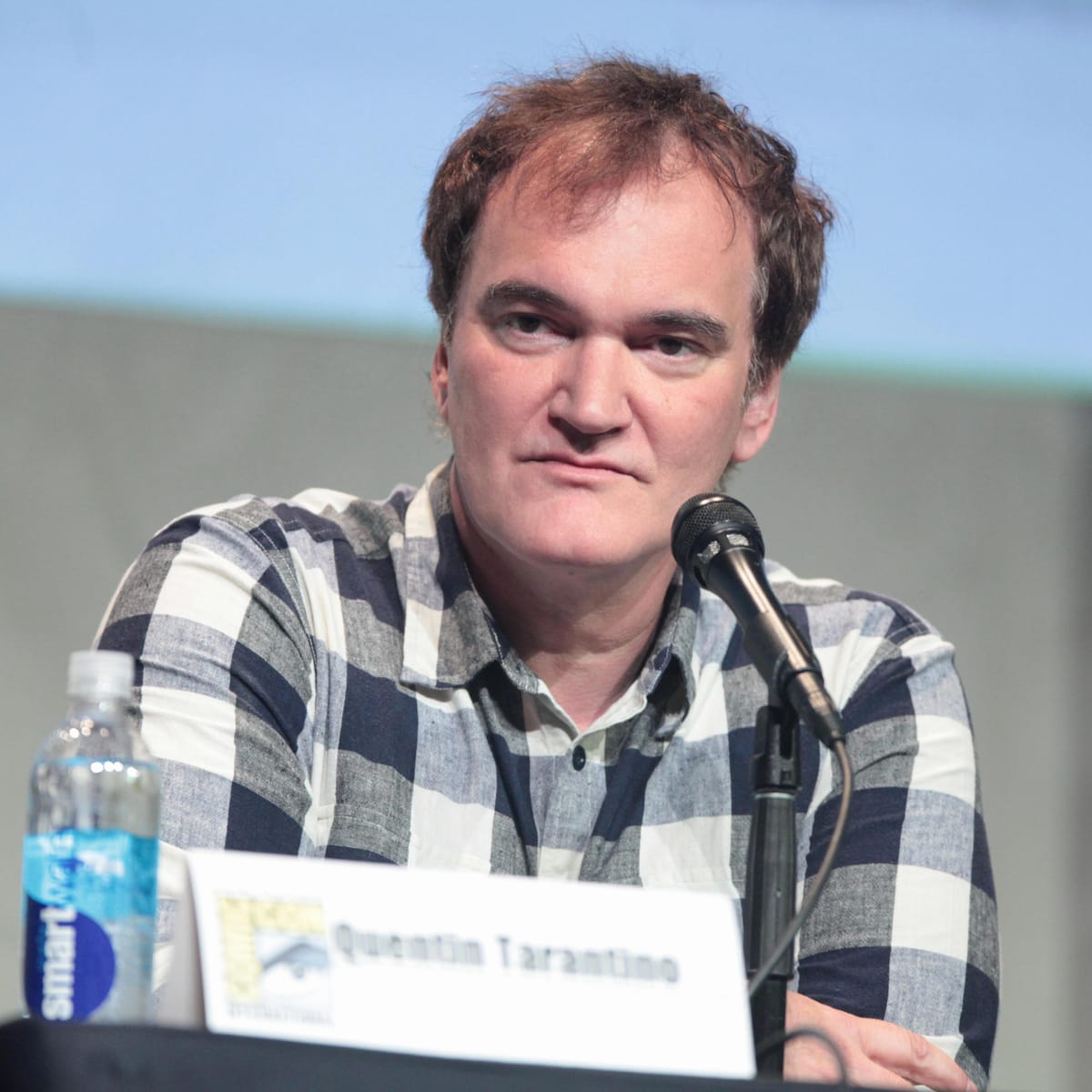 Quentin Tarantino speaking at a panel with microphone and name placard