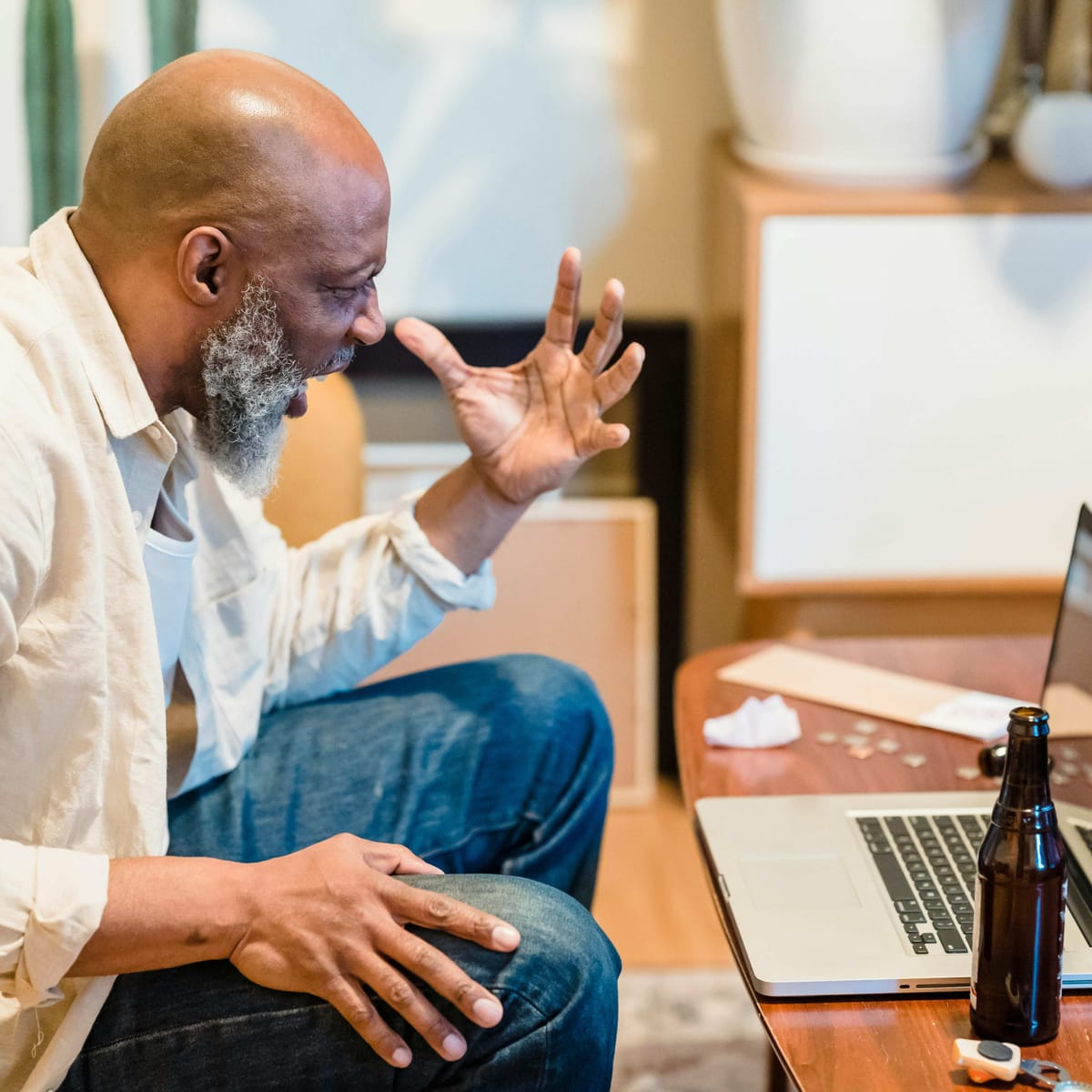 Man gesturing at laptop screen on coffee table, beer bottles nearby