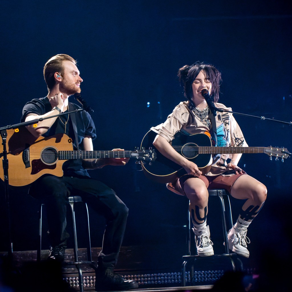 Billie Eilish and brother Finneas performing acoustic set on stage.